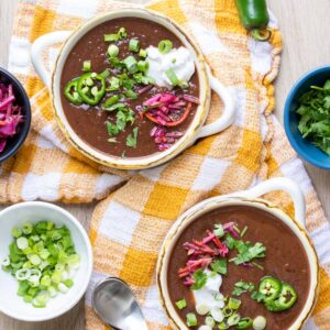 Two soup bowls with black bean soup and topped with sour cream, jalapeños, onions and cabbage