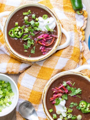 Two soup bowls with black bean soup and topped with sour cream, jalapeños, onions and cabbage