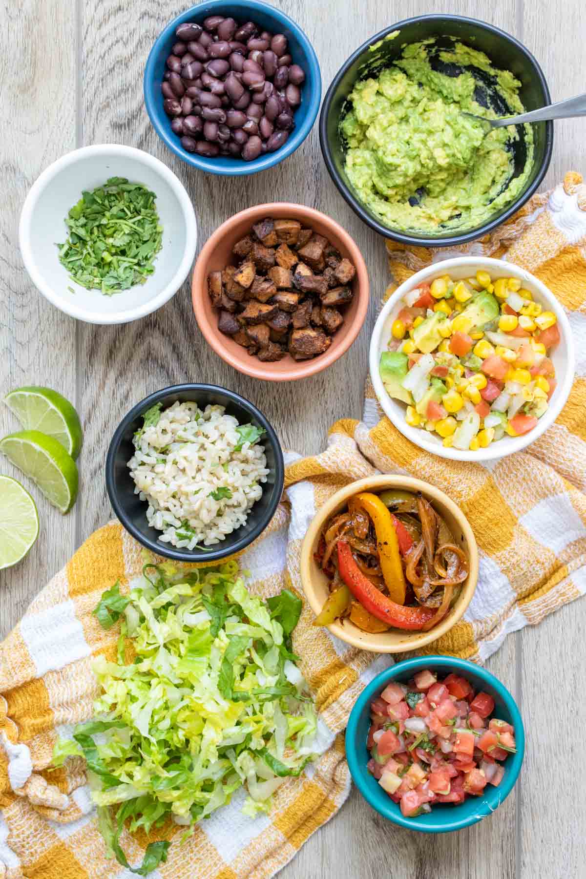 Different colored bowls on a checkered towel filled with ingredients to build a burrito bowl.