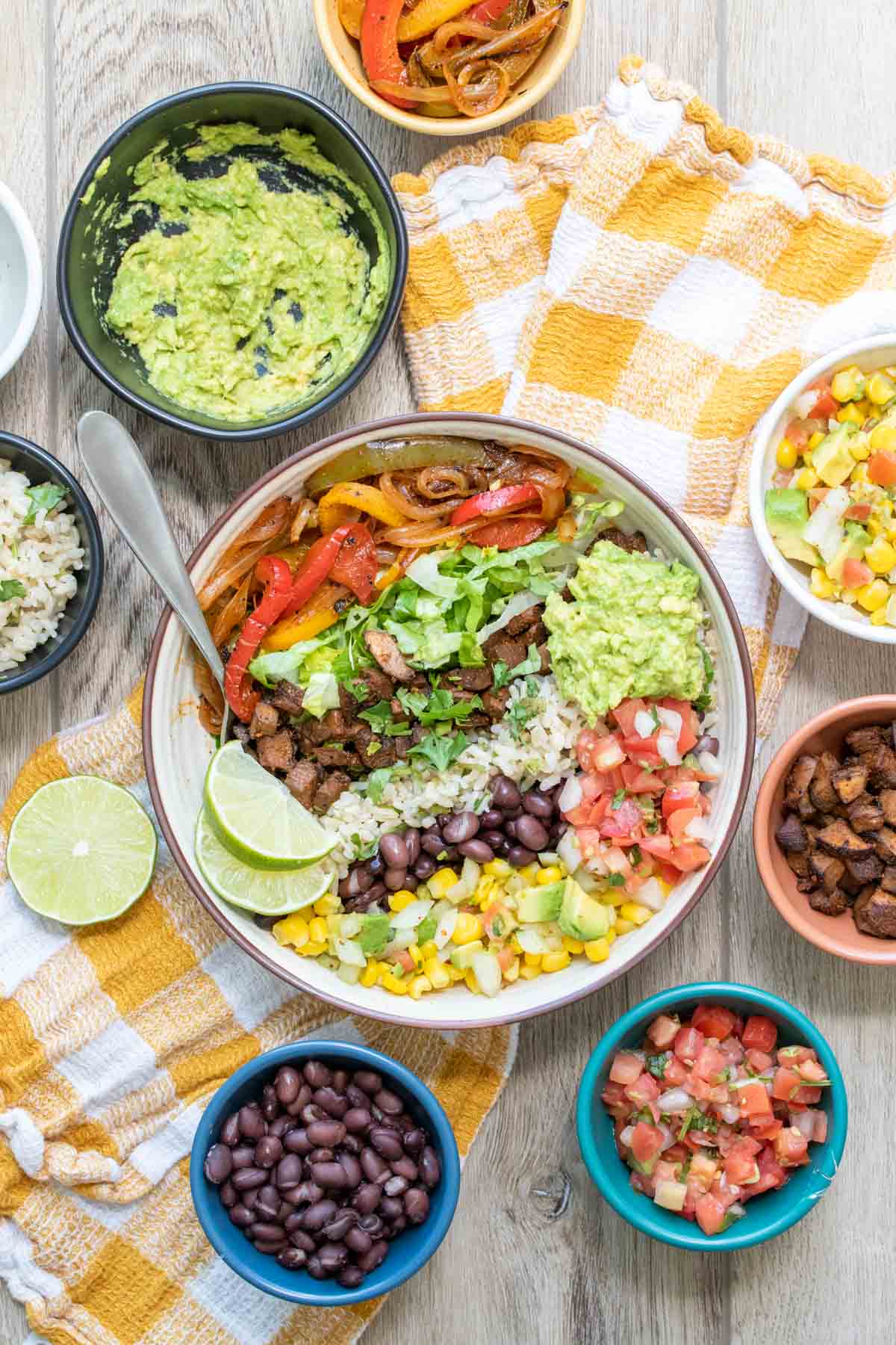 Bowl with piles of ingredients liked up to make a burrito bowl surrounded by small bowls of ingredients