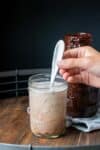 Hand using a spoon to mix chocolate into milk in a glass jar