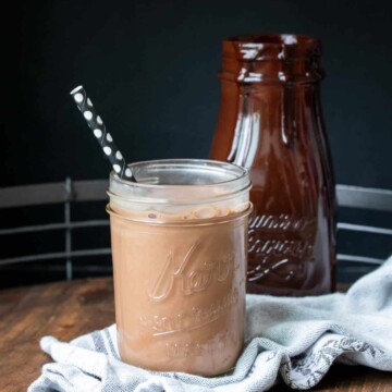 A glass jar filled with chocolate milk and a black straw