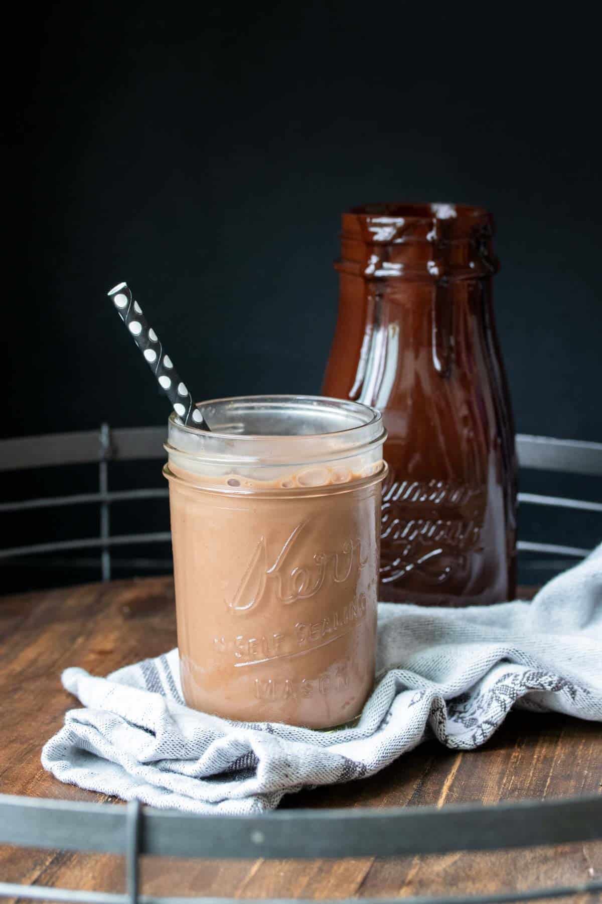 A glass jar filled with chocolate milk and a black straw