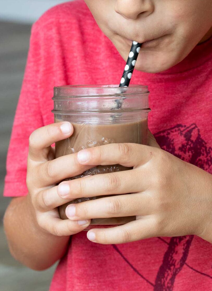 Boy holding a jar of chocolate milk and drinking it through a straw