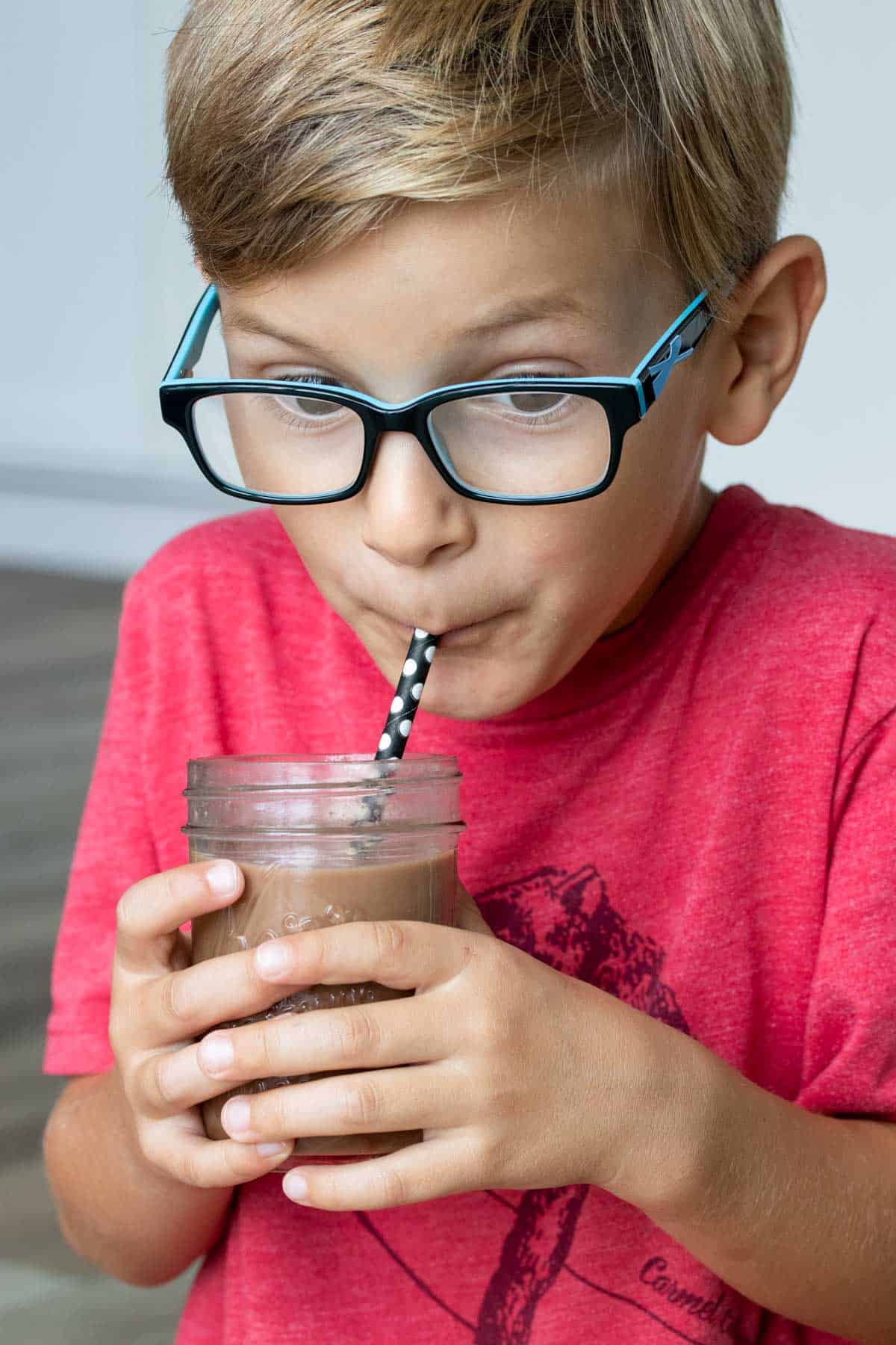 Boy holding a jar of chocolate milk and drinking it through a straw