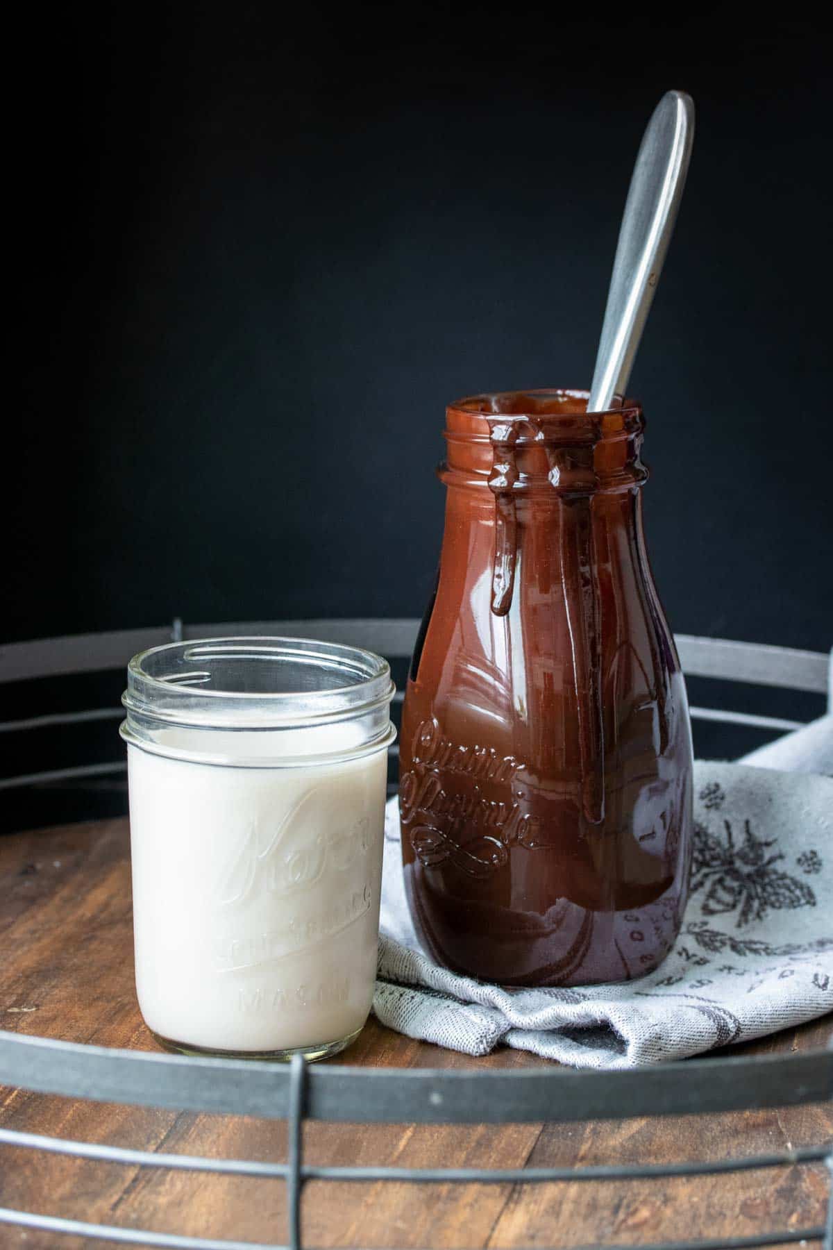 Glass of milk next to a tall glass bottle of chocolate syrup
