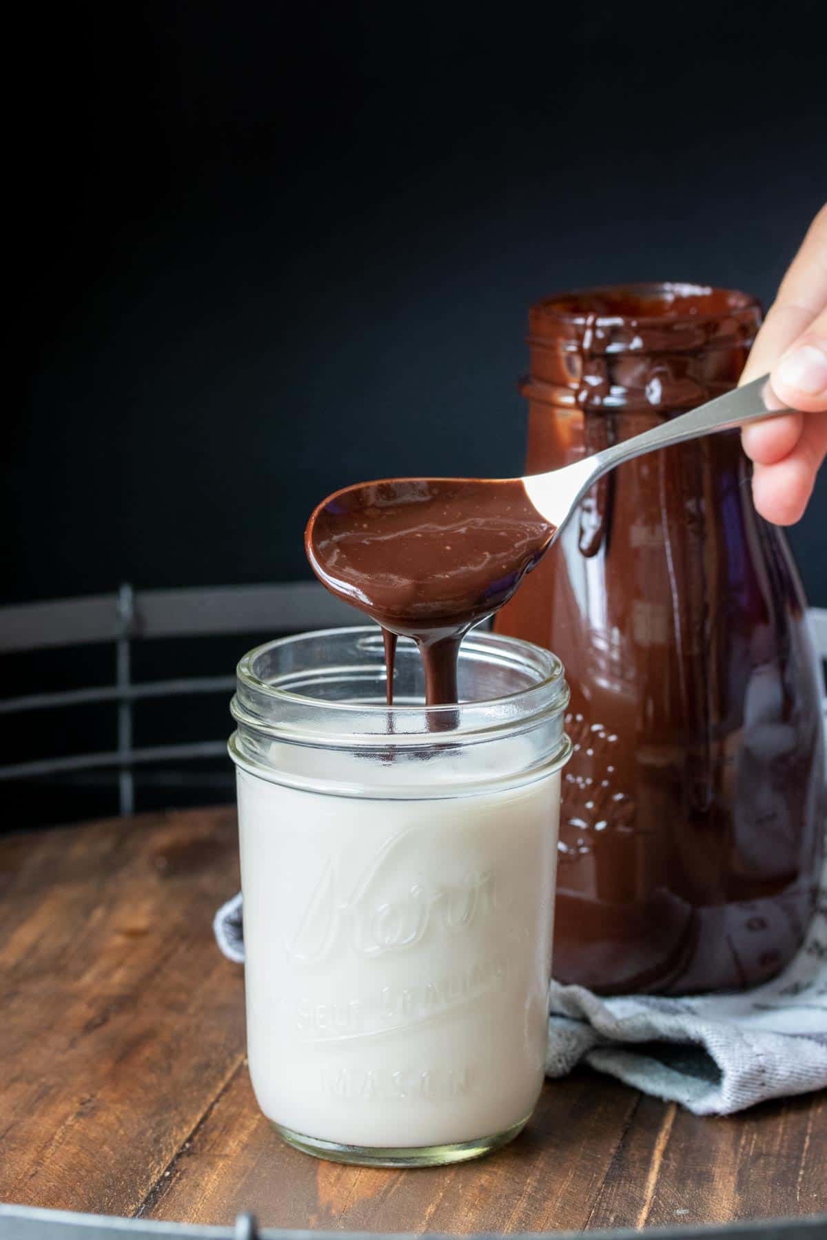 Spoon putting chocolate syrup into a glass of milk with a spoon