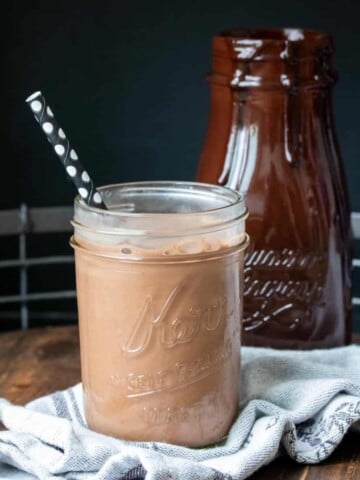 Chocolate milk in a glass jar with a black dotted straw on a wooden surface