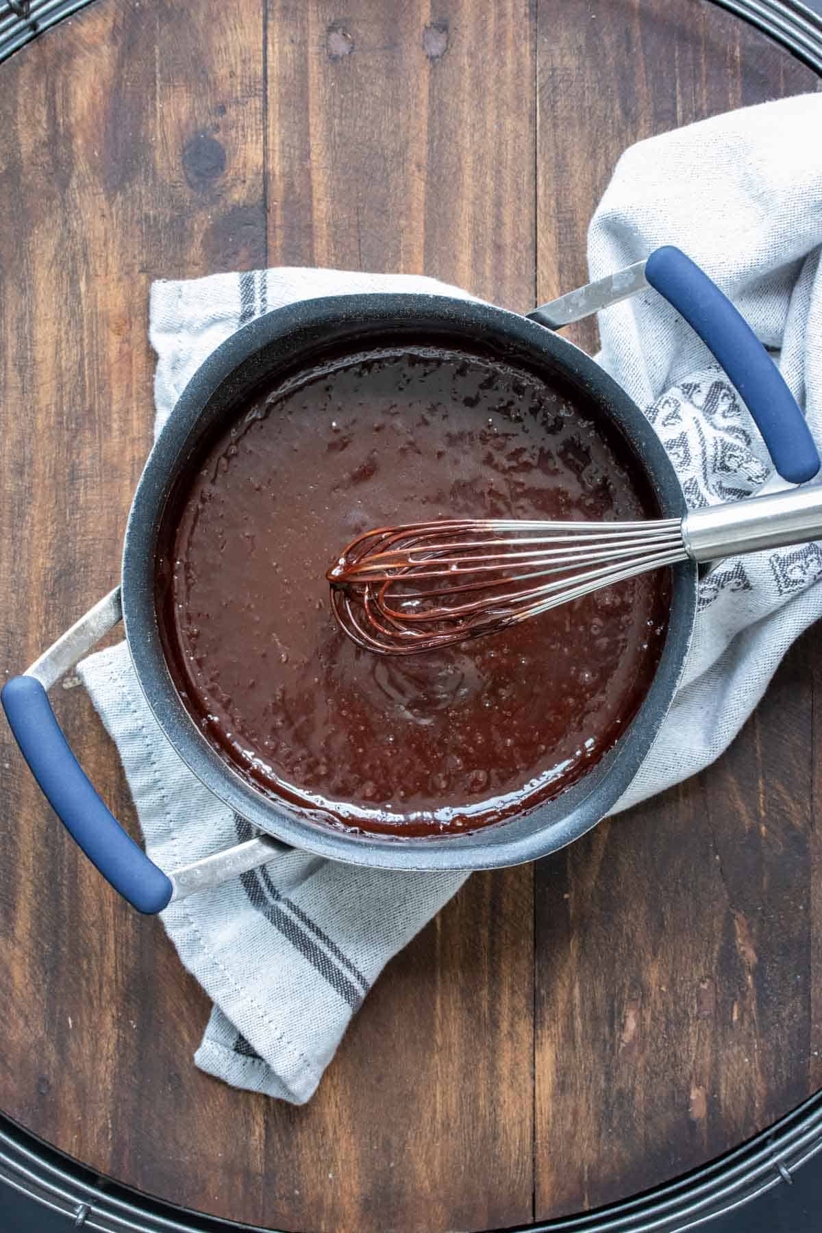 Whisk mixing thick chocolate sauce in a pot.