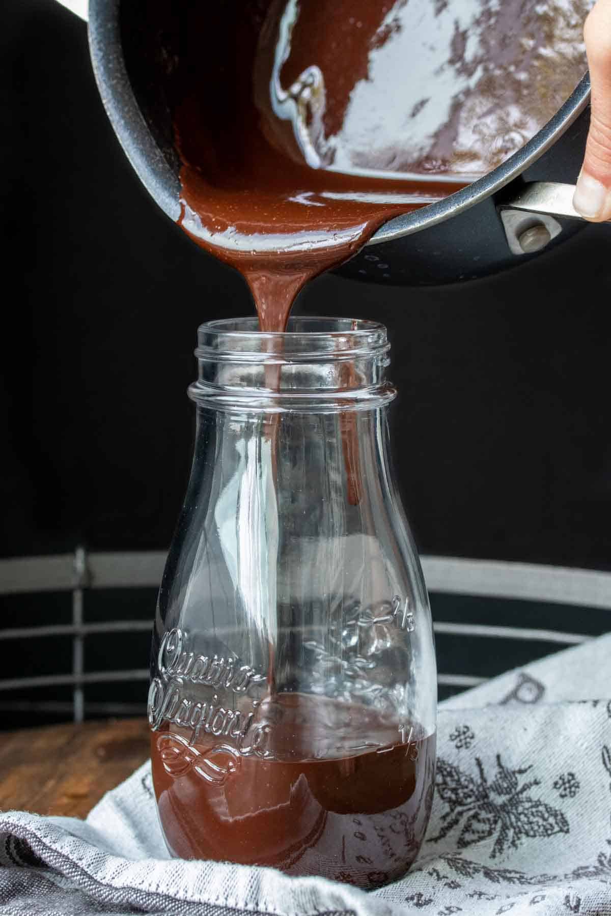 Chocolate sauce pouring into a glass bottle from a pot.