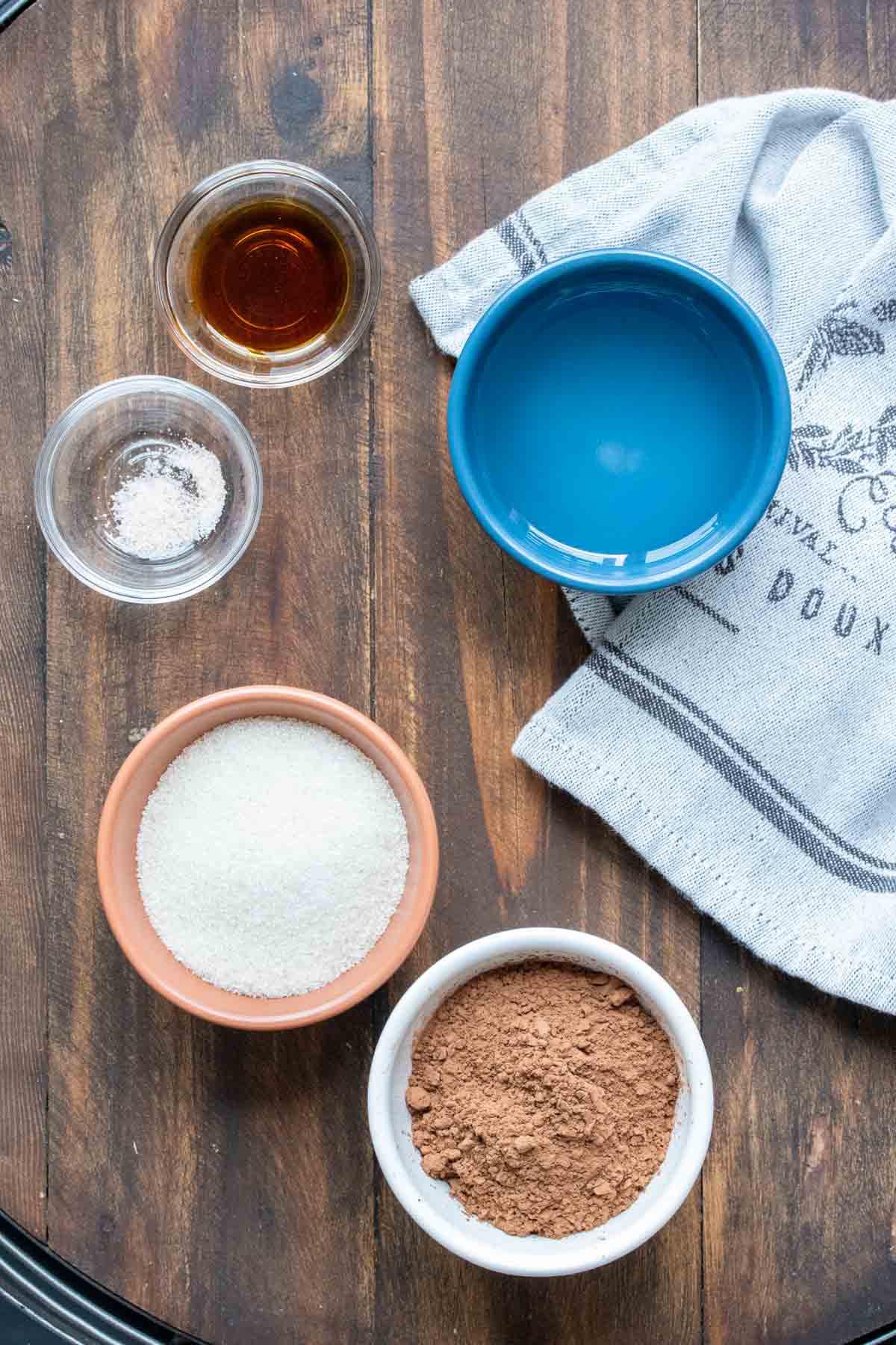 Ingredients needed to make homemade chocolate syrup in bowls in a wooden surface