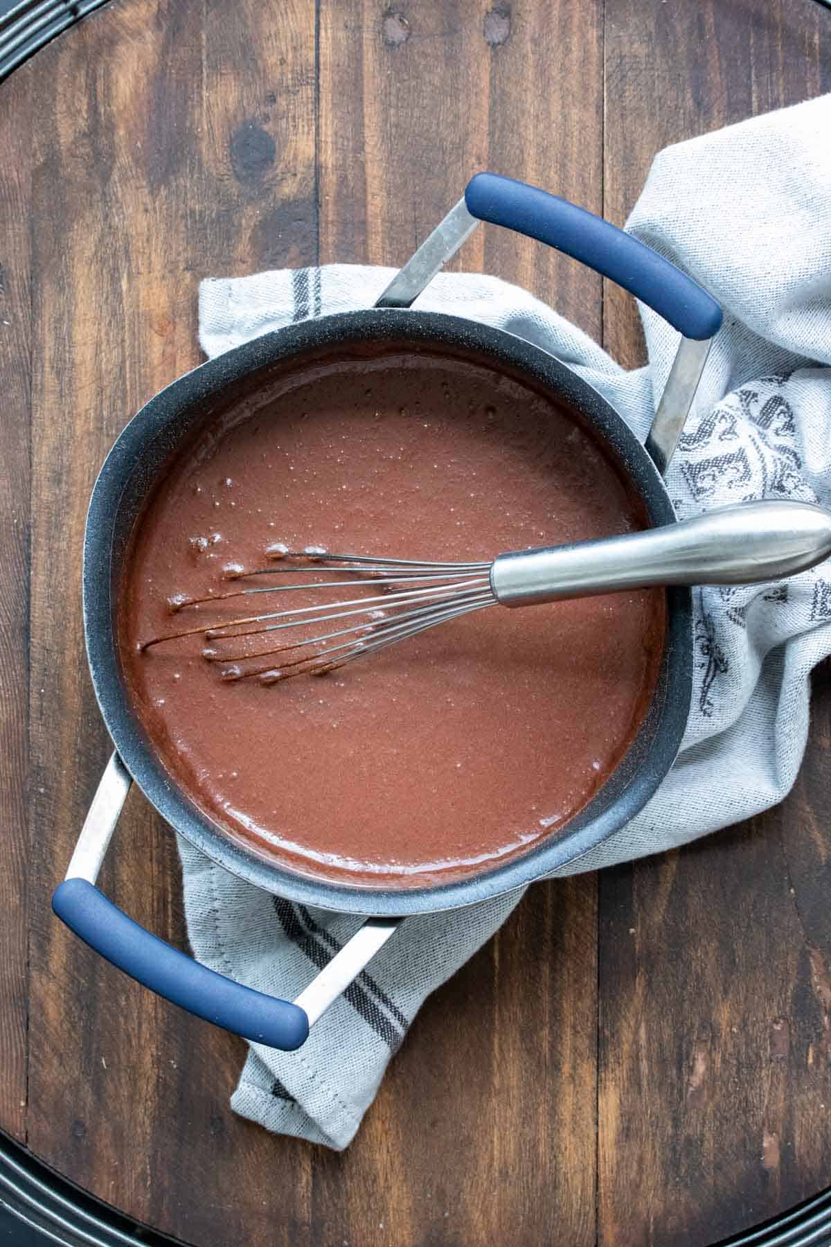 Whisk mixing chocolate looking liquid in a pot.