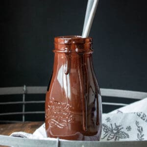 Glass bottle with chocolate syrup on a grey towel.