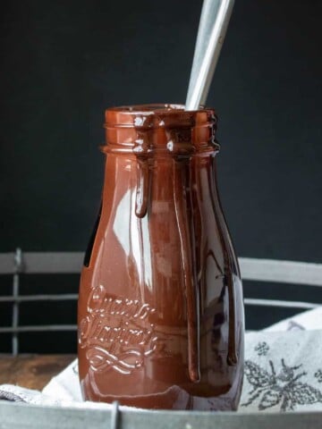 Glass bottle with chocolate syrup on a grey towel.