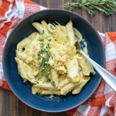 Top view of a blue bowl with penne pasta mixed with creamy butternut squash sauce and topped with fresh thyme