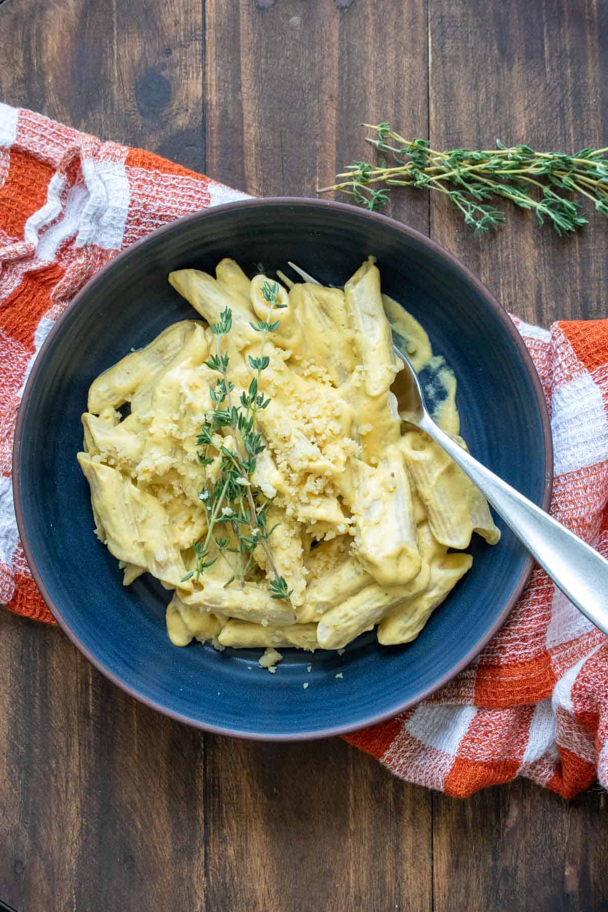 Top view of a blue bowl with penne pasta mixed with creamy butternut squash sauce and topped with fresh thyme