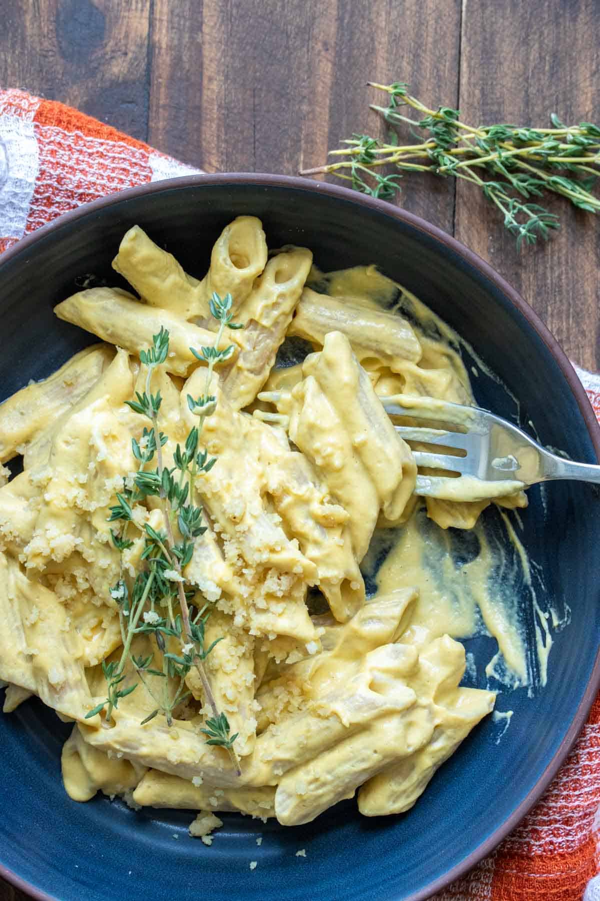 Fork getting a bite of pasta with creamy butternut squash sauce from a blue bowl