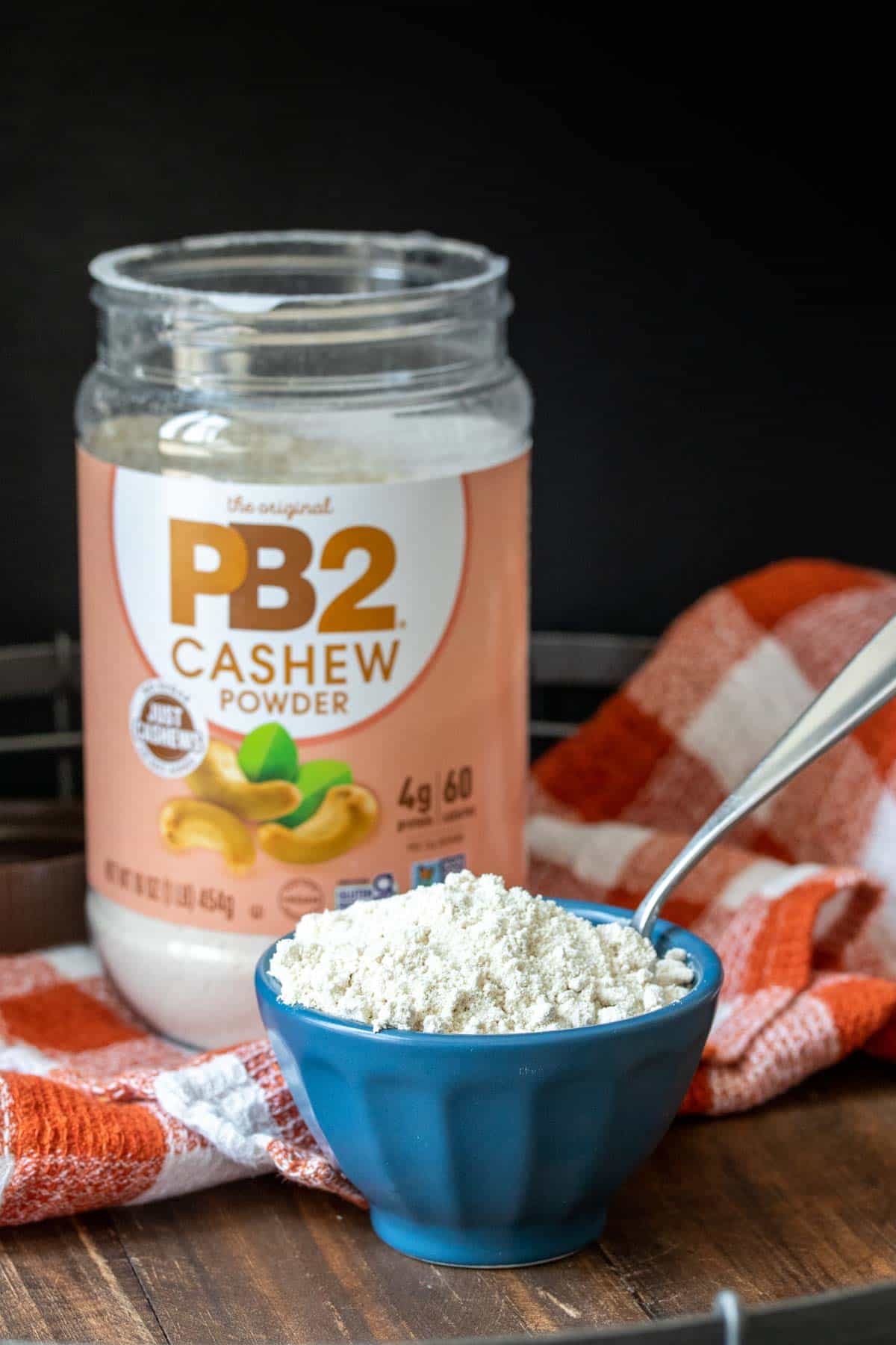 A blue bowl with powdered cashew in it in front of the container