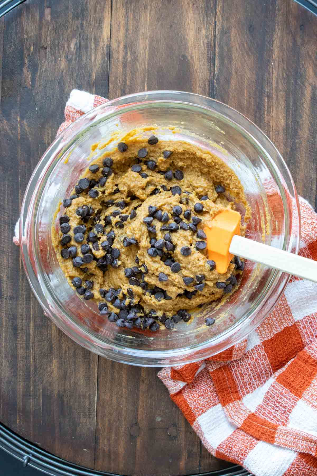 Chocolate chips being mixed into pumpkin cookie batter in a glass bowl