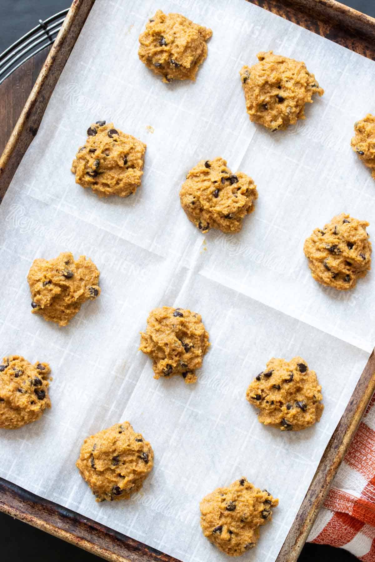 Raw spoonfuls of pumpkin chocolate chip cookies on a parchment lined cookie sheet