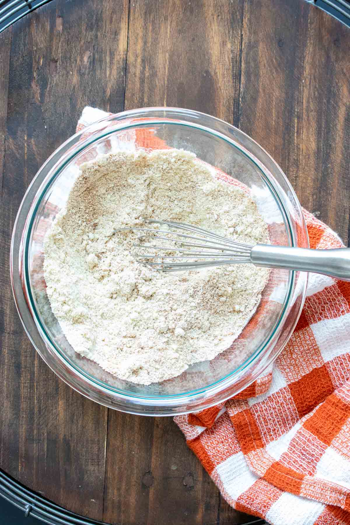 Whisk mixing flours in a glass bowl sitting on an orange checkered towel