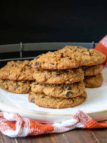 Cream colored plate sitting on an orange checkered towel piled with chocolate chip cookies