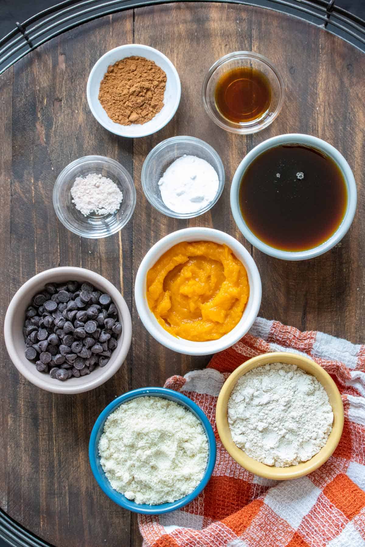 Top view of colored bowls with ingredients to make pumpkin chocolate chip cookies on a wooden surface