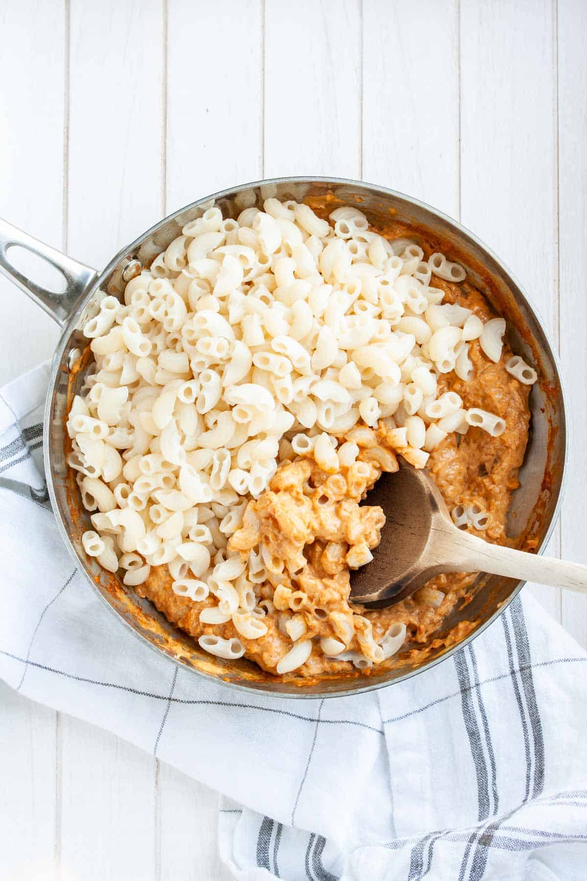 Saute pan with macaroni and an orange sauce being mixed with a wooden spoon