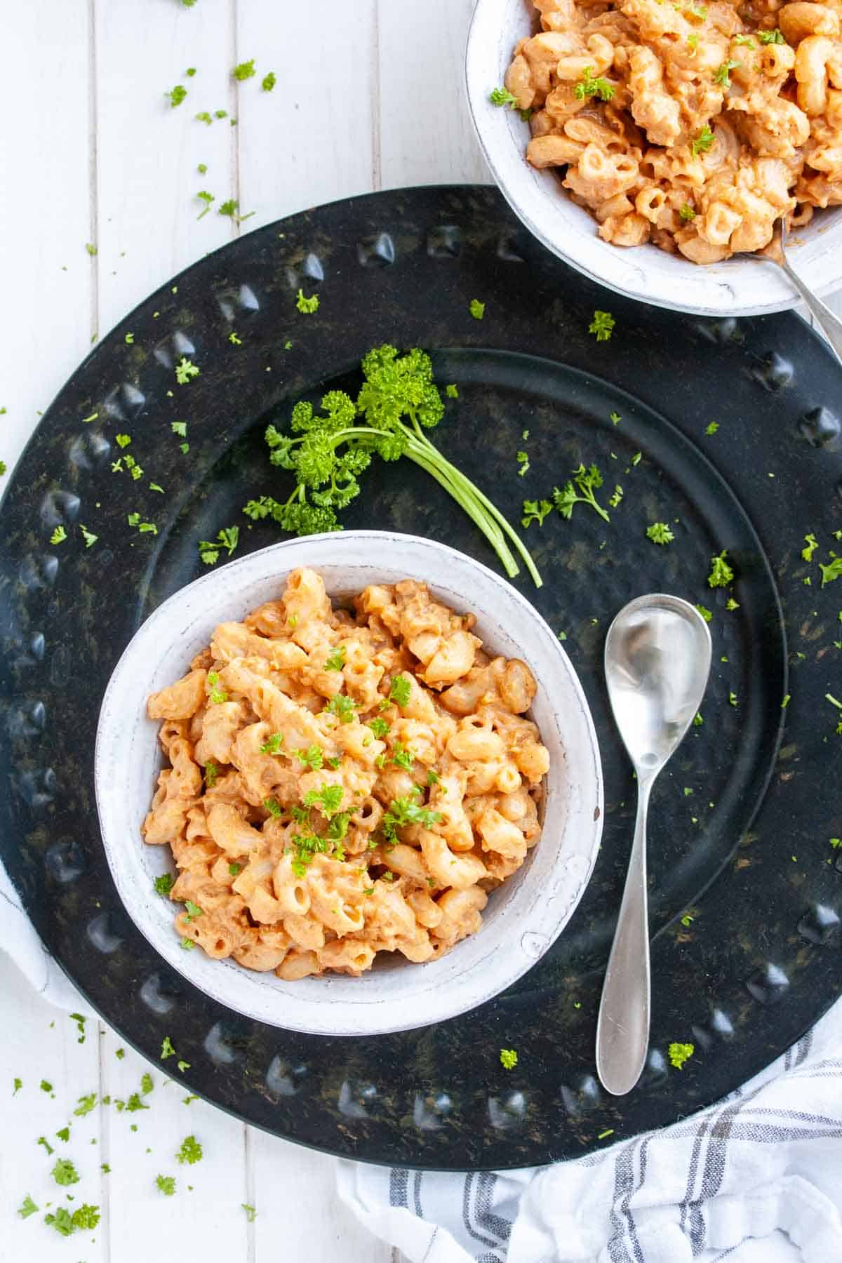 Black platter with a white bowl filled with cheesy hamburger macaroni