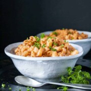 Two white bowls on a black platter filled with hamburger helper pasta topped with parsley