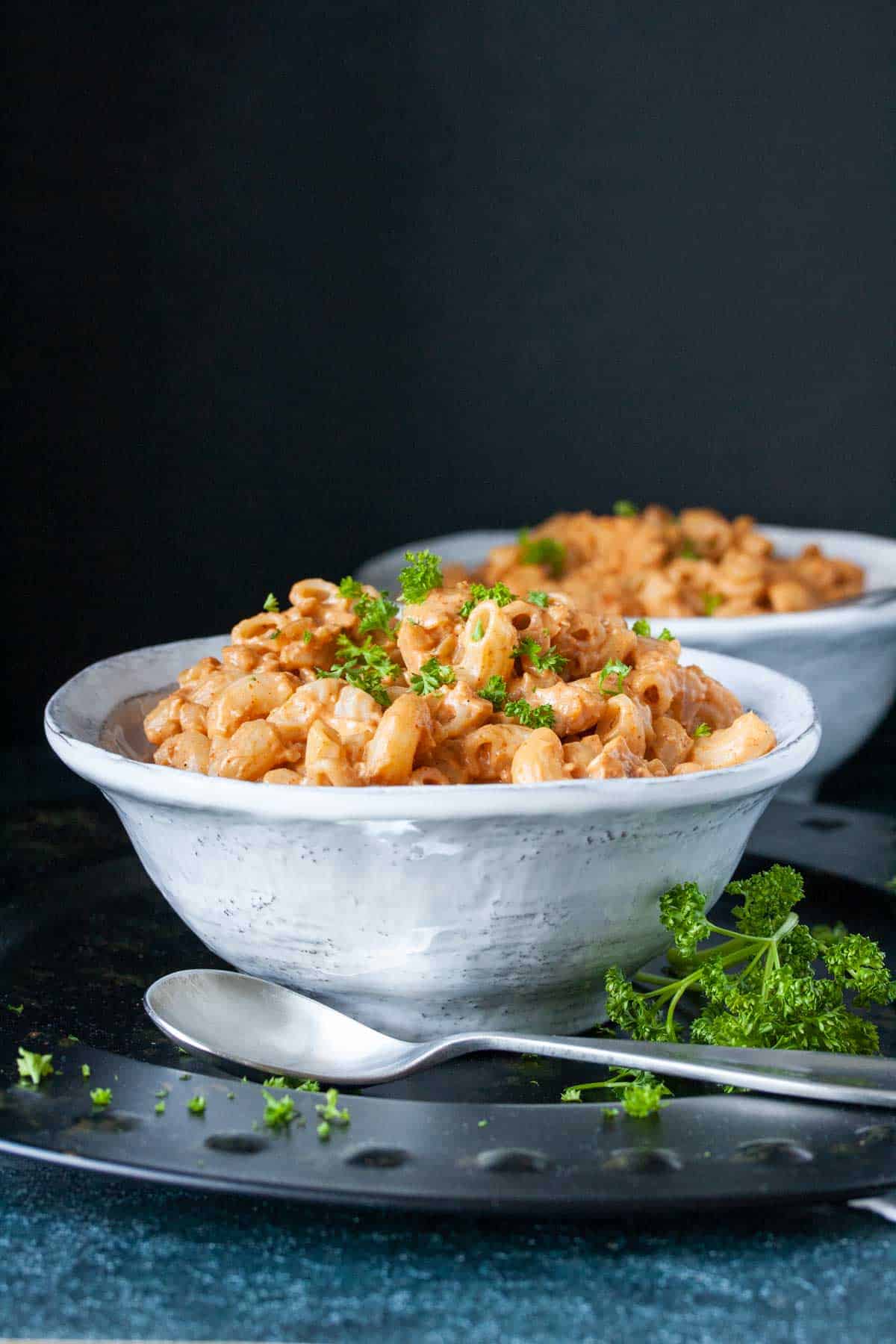 Two white bowls on a black platter filled with hamburger helper pasta topped with parsley