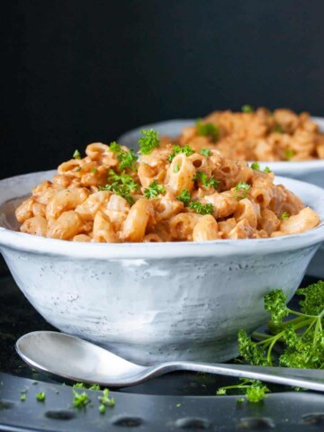 White bowl on a black platter with a spoon on it filled with hamburger helper macaroni and chopped parsley