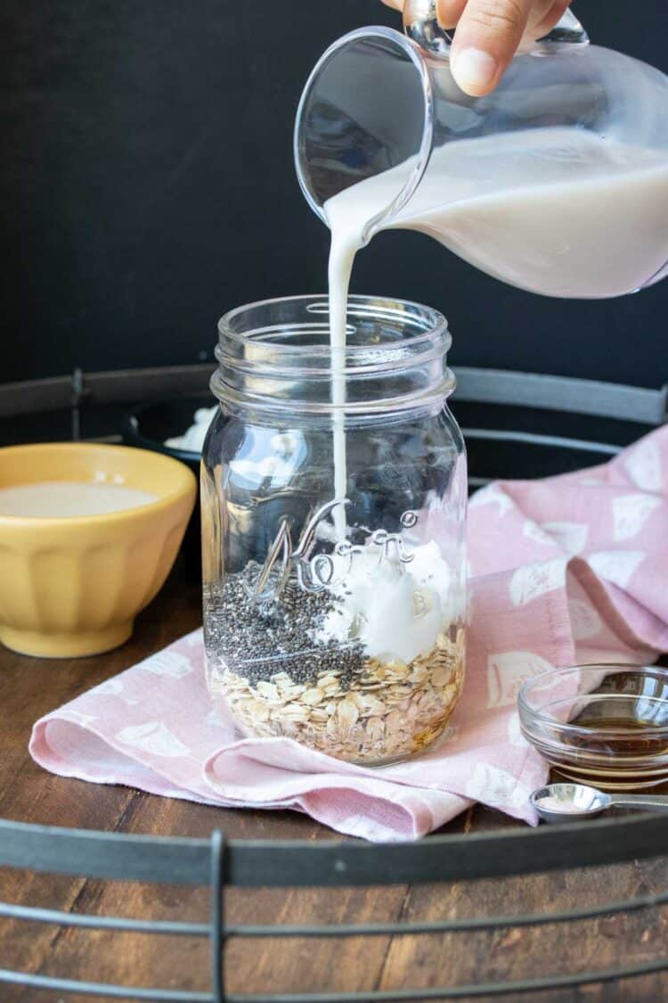 Milk pouring out of a glass pitcher into a jar with oats and chia seeds