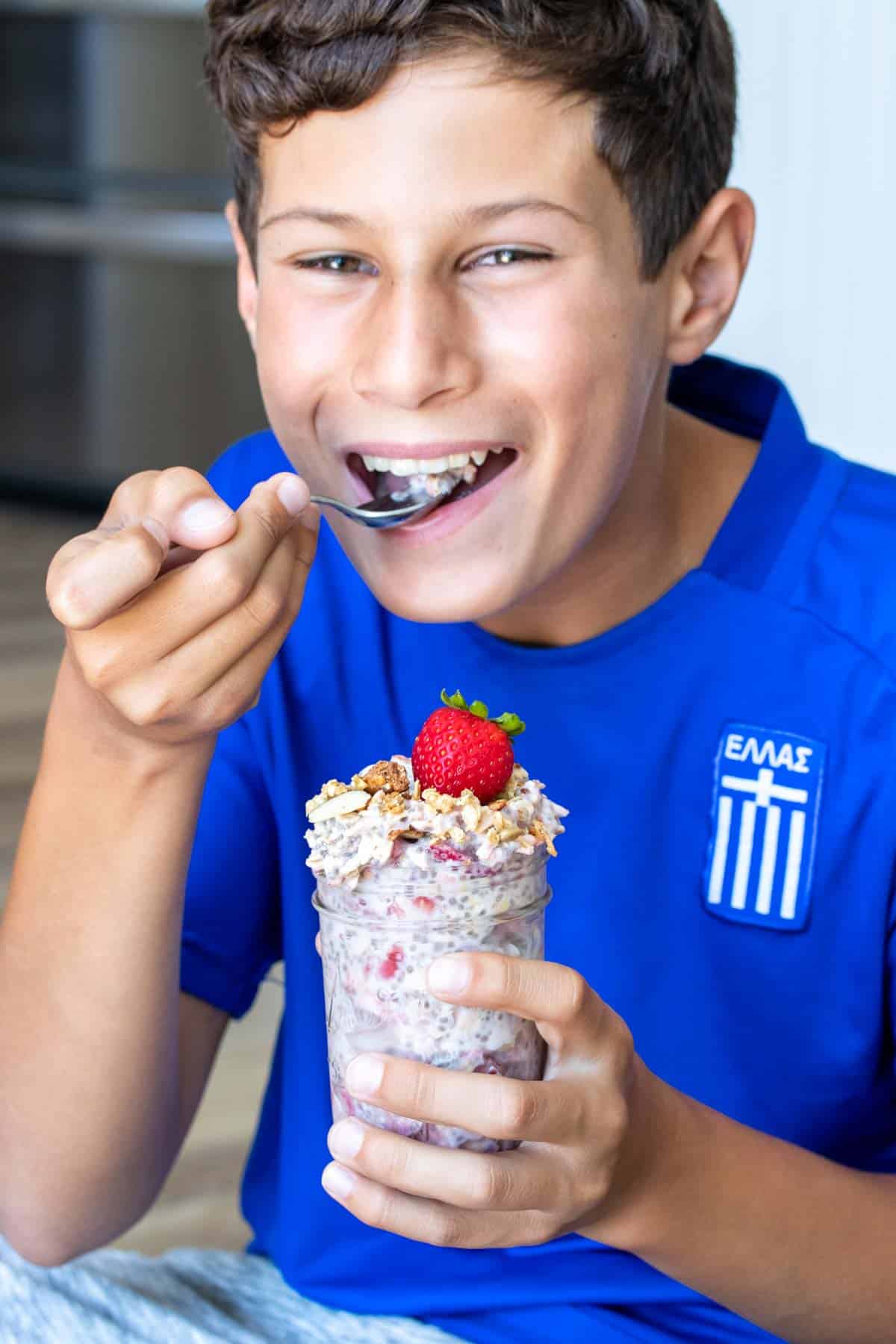 Boy in blue shirt smiling and eating from a jar of overnight oats