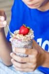 Close up of a boy getting a bite from a jar of overnight oats topped with fresh strawberries