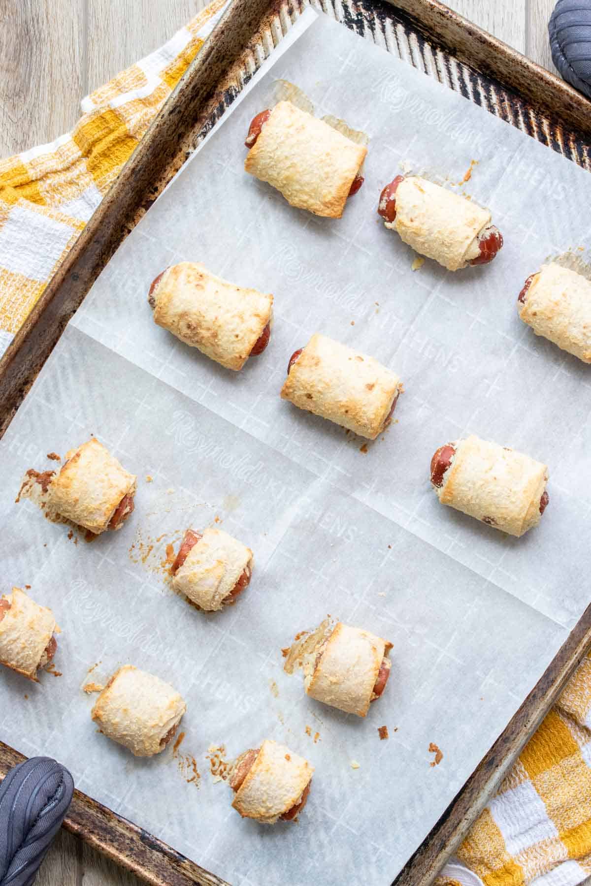 Baked pigs in a blanket on a parchment lined baking sheet.