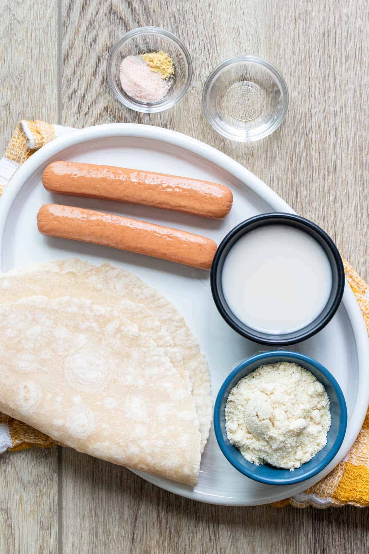 Plate with ingredients needed to make homemade pigs in a blanket with tortilla wraps