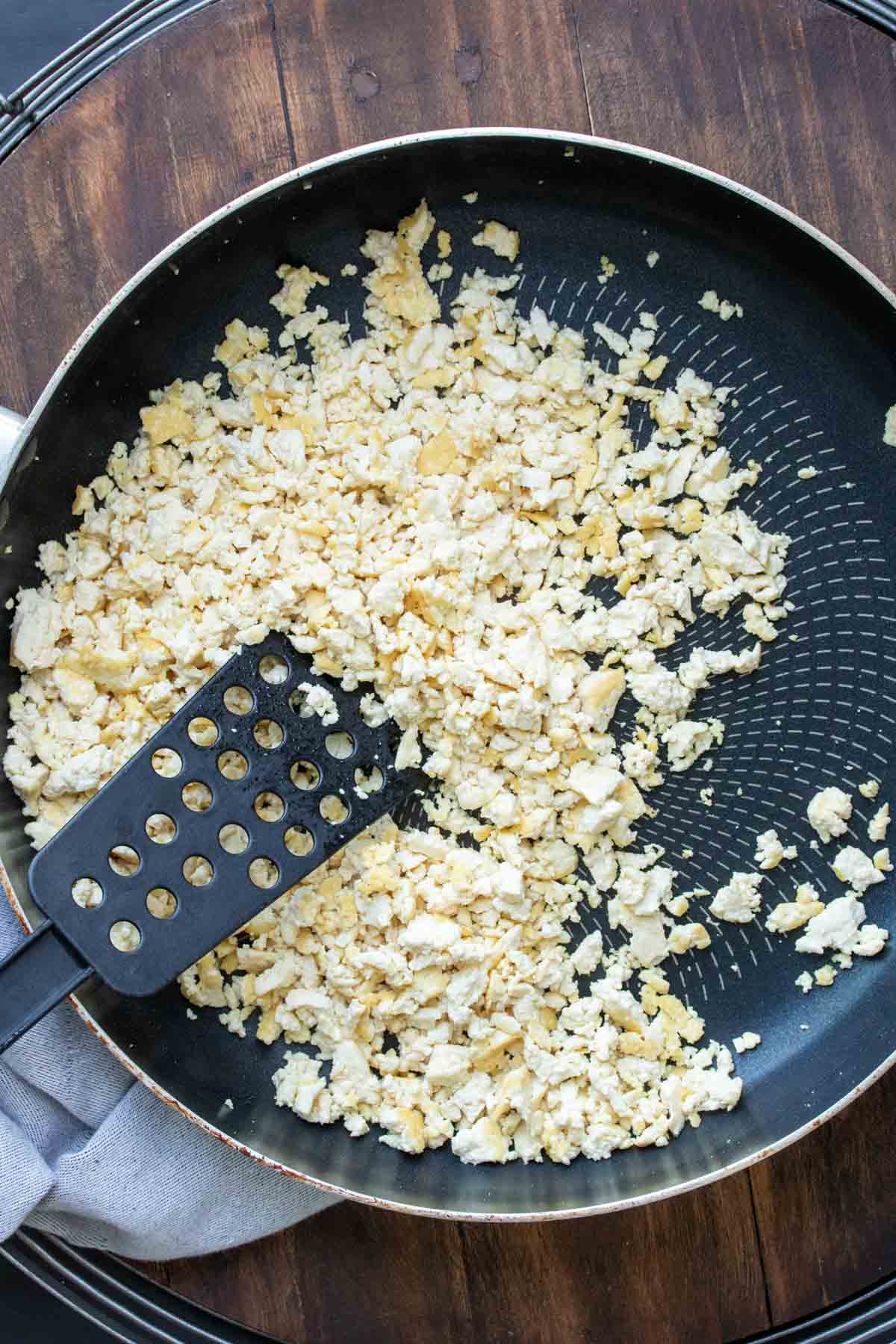 Spatula cooking crumbled tofu in a black pan.