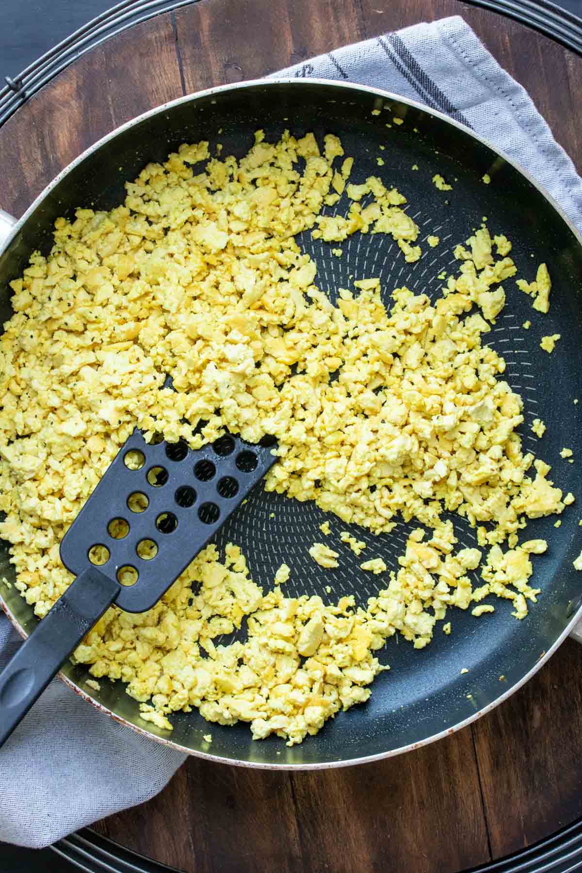 Spatula cooking yellow crumbled tofu in a pan.