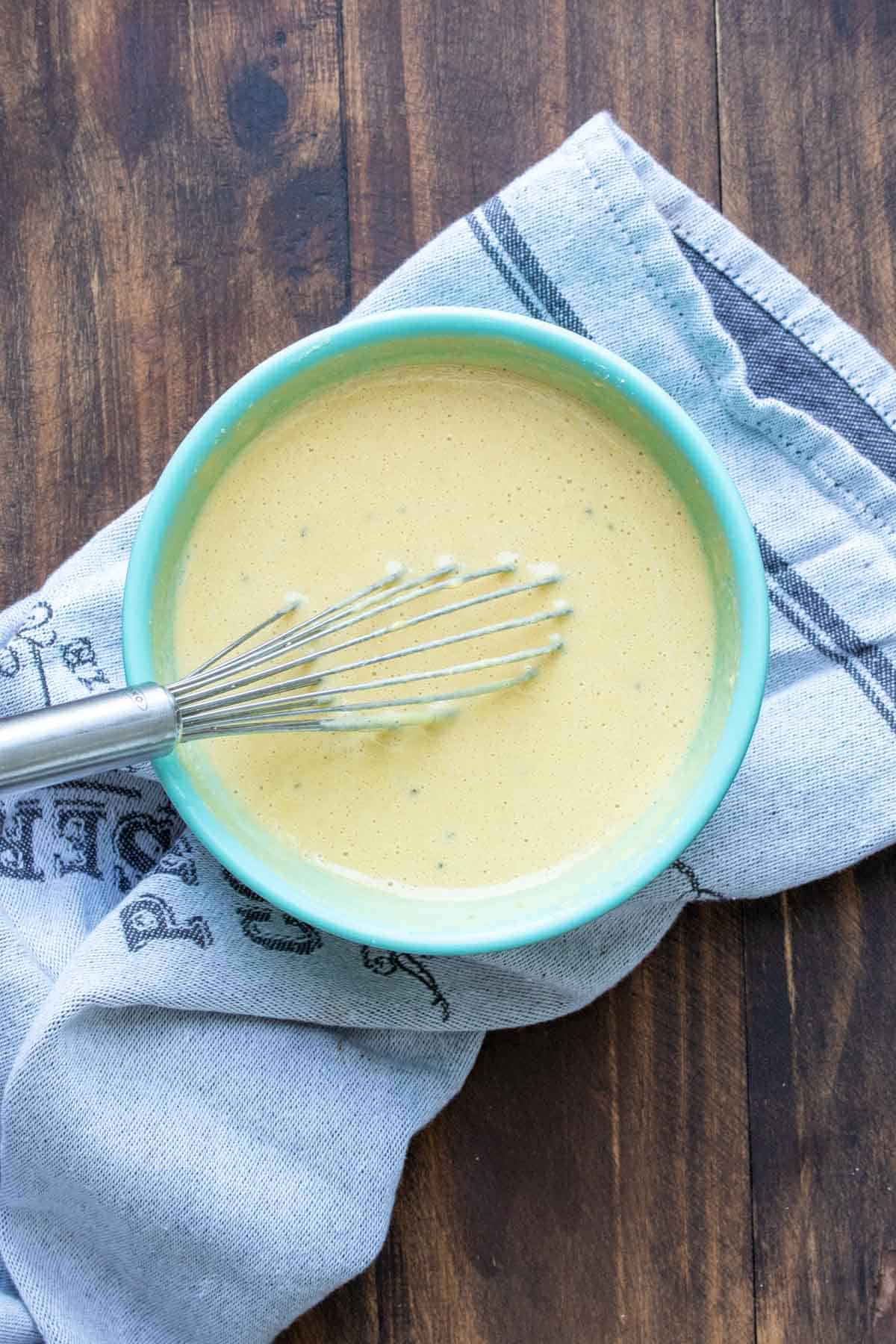 Whisk mixing a light yellow liquid in a turquoise bowl.