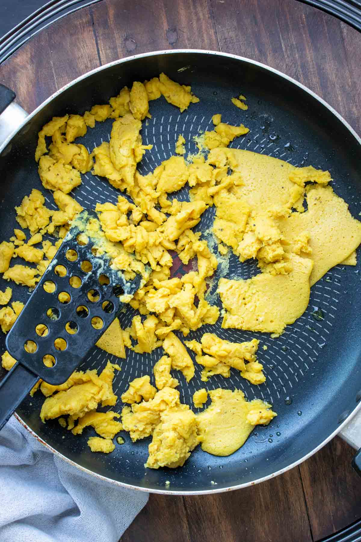 Spatula breaking up cooked chickpea pancake in a pan