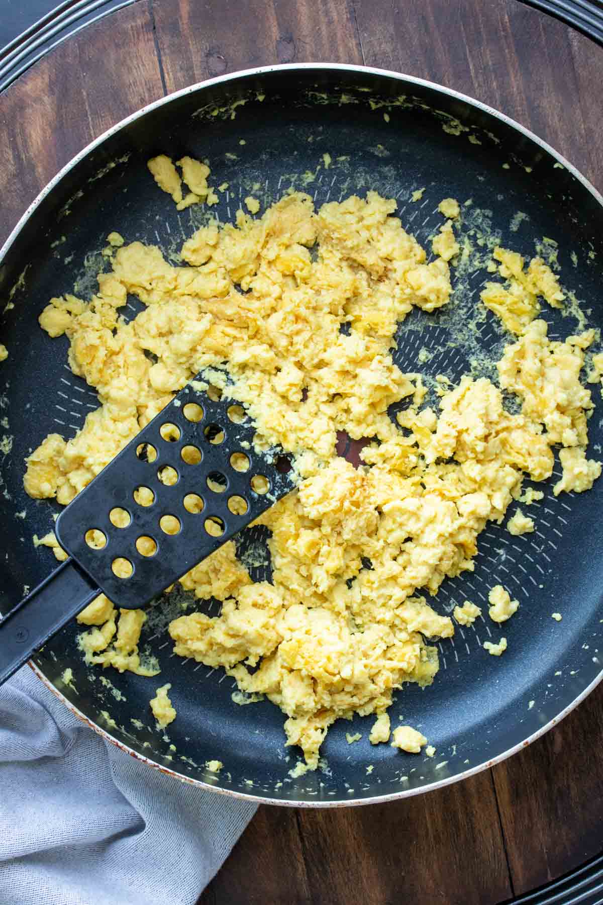 Spatula cooking scrambled eggs in a pan.