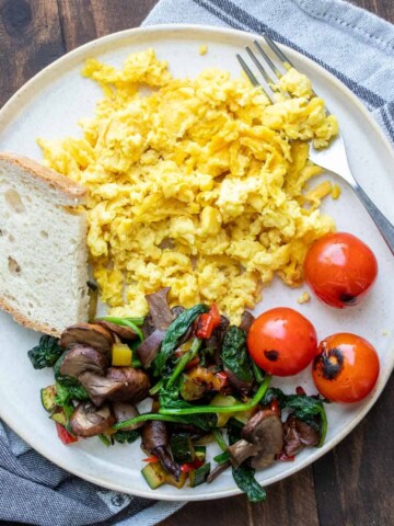 Mixed veggies, toast and scrambled eggs on a cream colored plate.