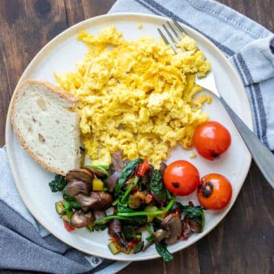 Mixed veggies, toast and scrambled eggs on a cream colored plate.