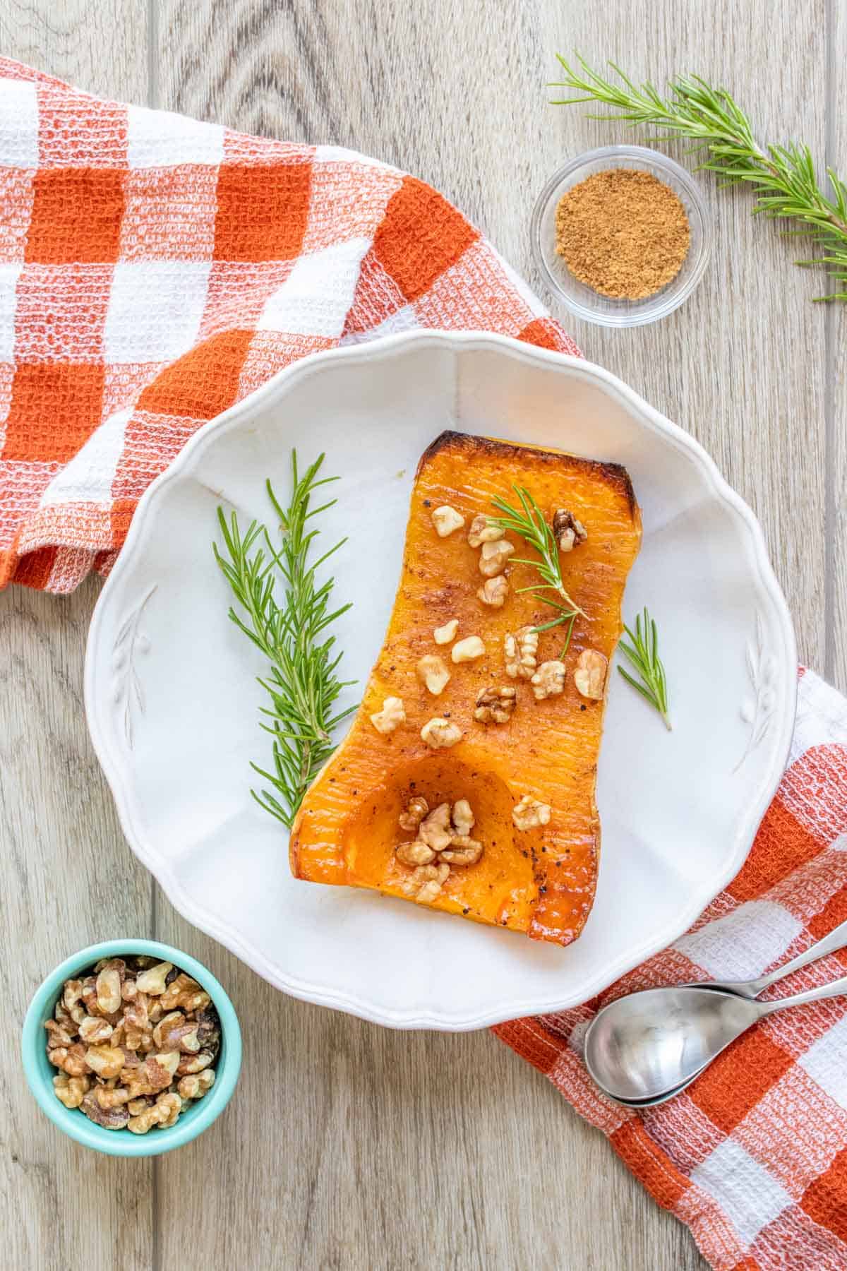 White bowl with a roasted half butternut squash with rosemary and nuts