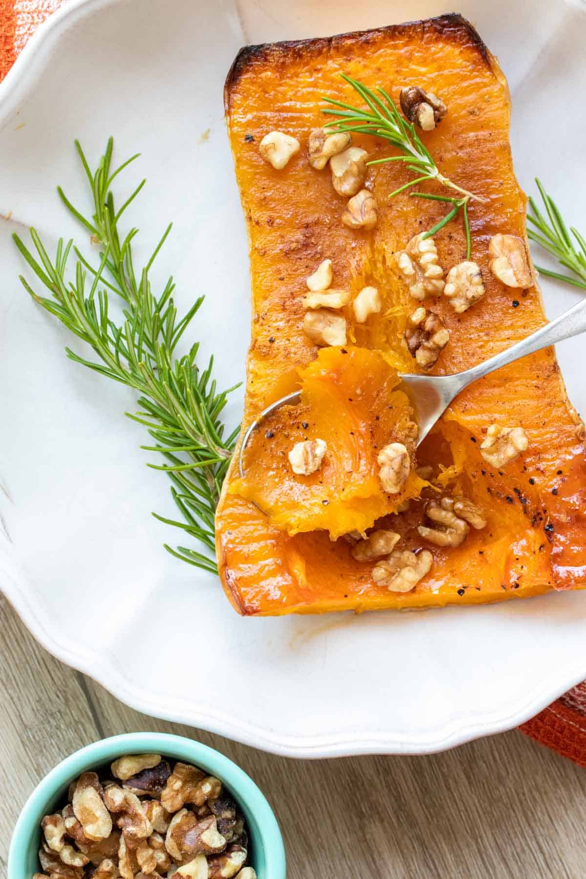 Spoon getting a scoop of roasted butternut squash sprinkled with nuts in a white plate.