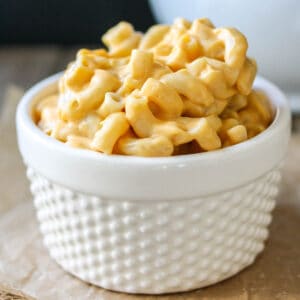 White bowl with a texture pattern sitting on parchment paper filled with orange mac and cheese.