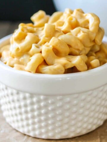 White bowl with a texture pattern sitting on parchment paper filled with orange mac and cheese.