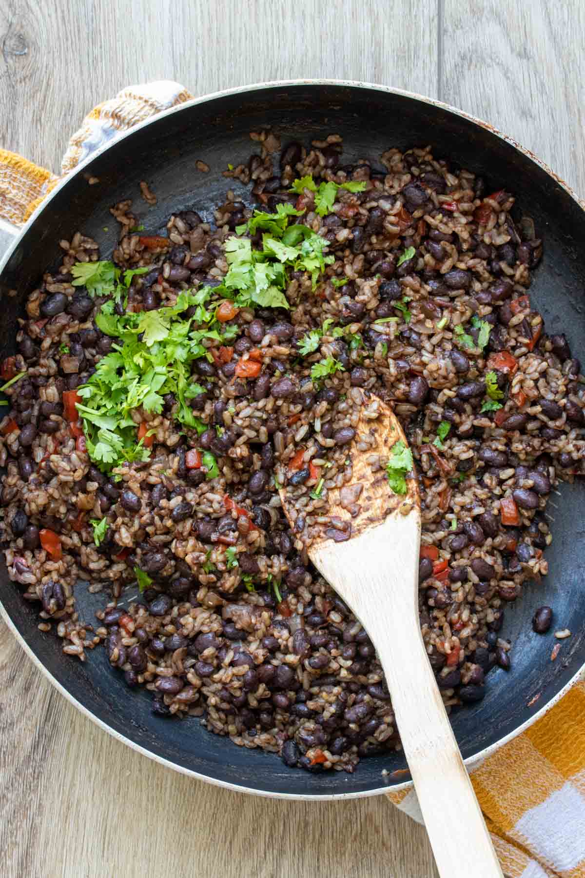 Cilantro being mixed into a black bean, rice and red pepper mix in a pan