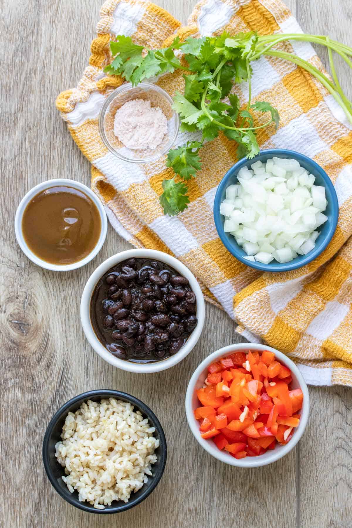 Bowls with beans, rice, onions, red pepper, green sauce, salt and cilantro on a yellow towel.